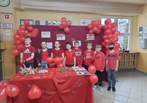 Dzieci w czerwonych strojach na tle balonów